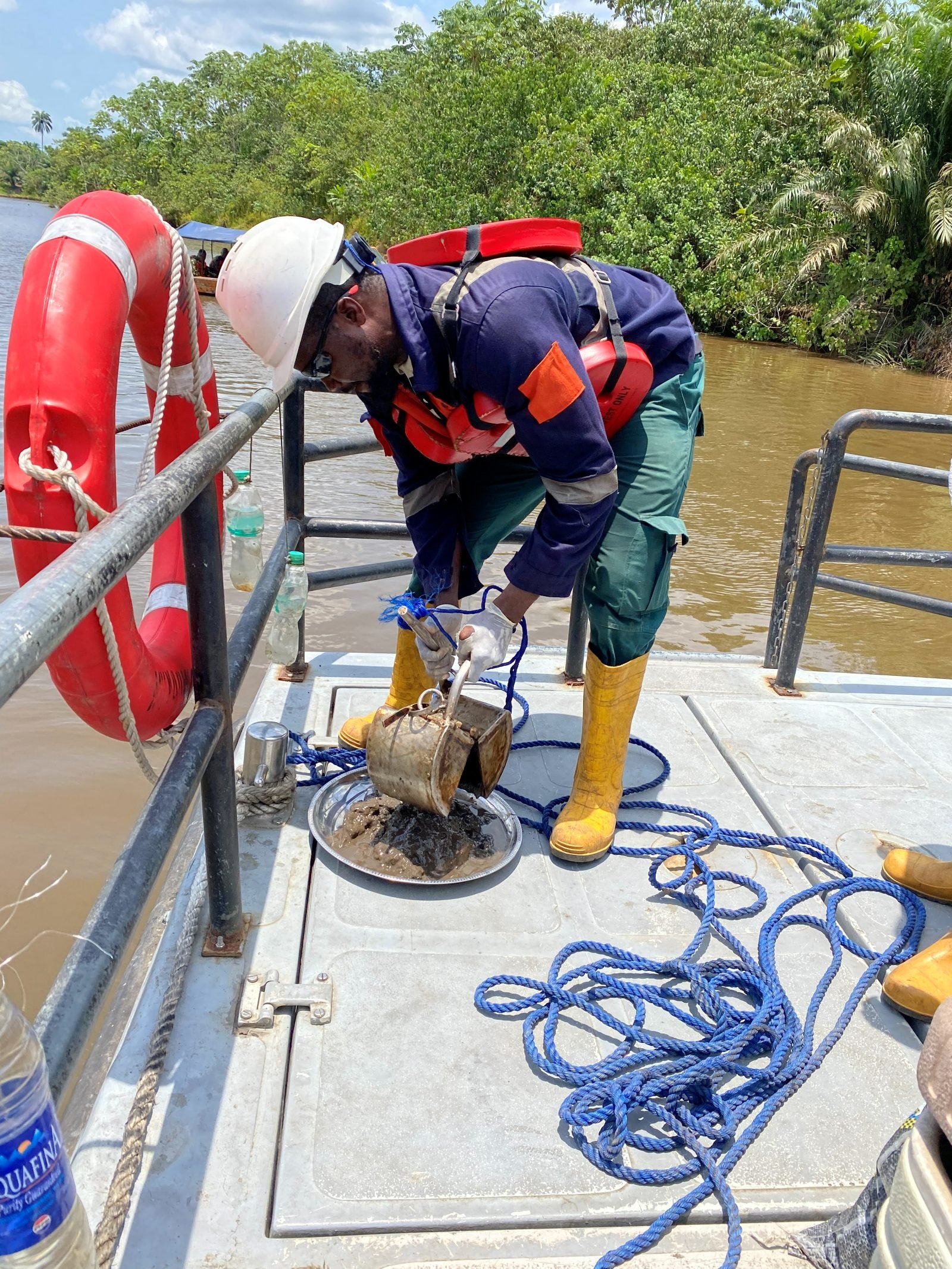 Engineer taking a surface-water and sediment sample from a boat on a Niger Delta river