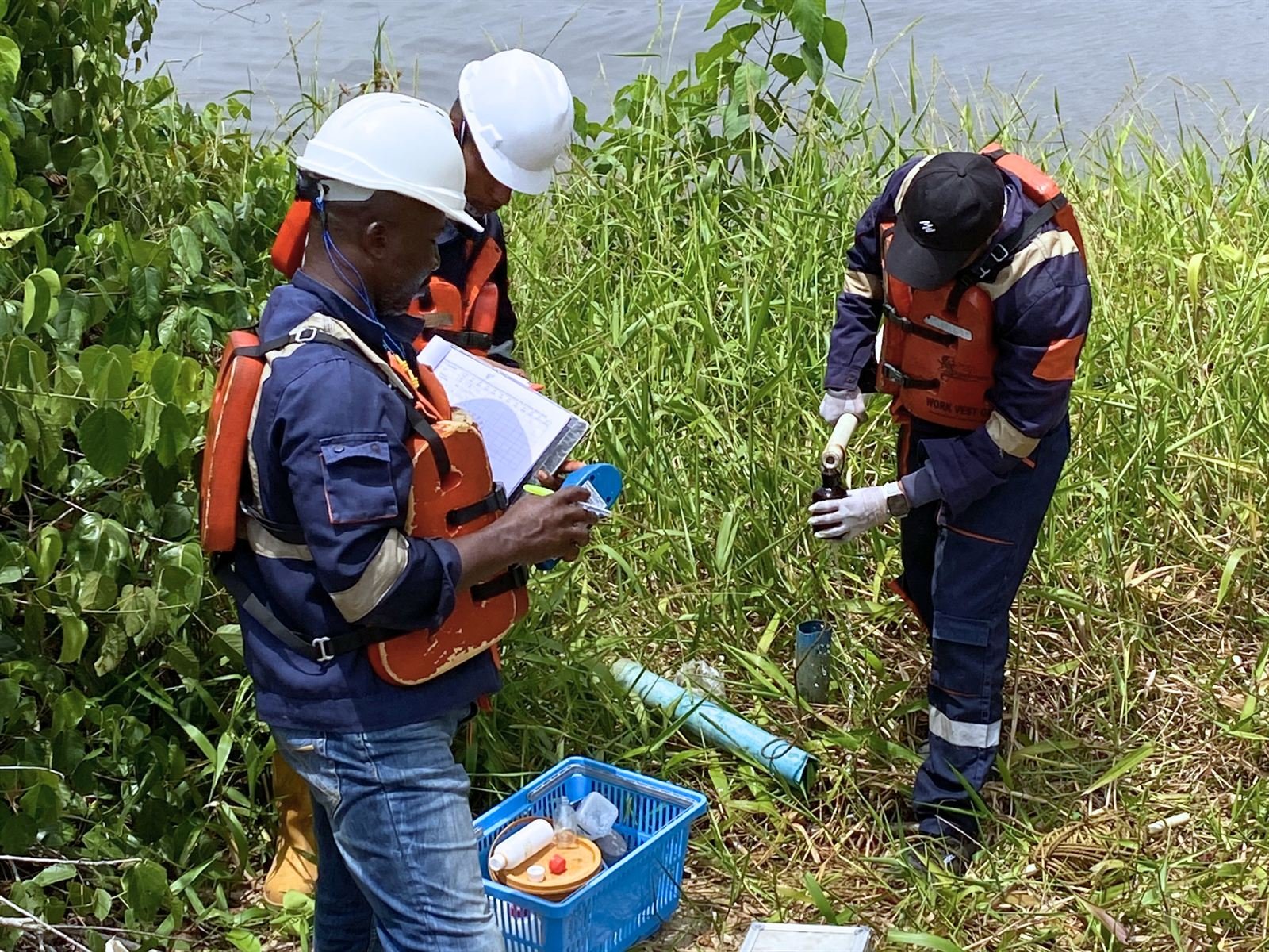 Field team collecting a water sample from vegetation beside a waterway